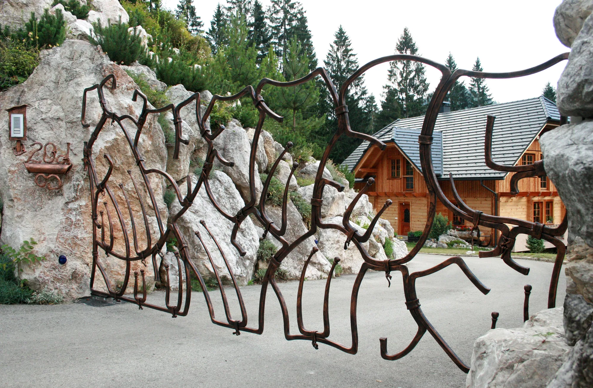 Ein Tor aus freien Linien vor einem Alpenhaus.